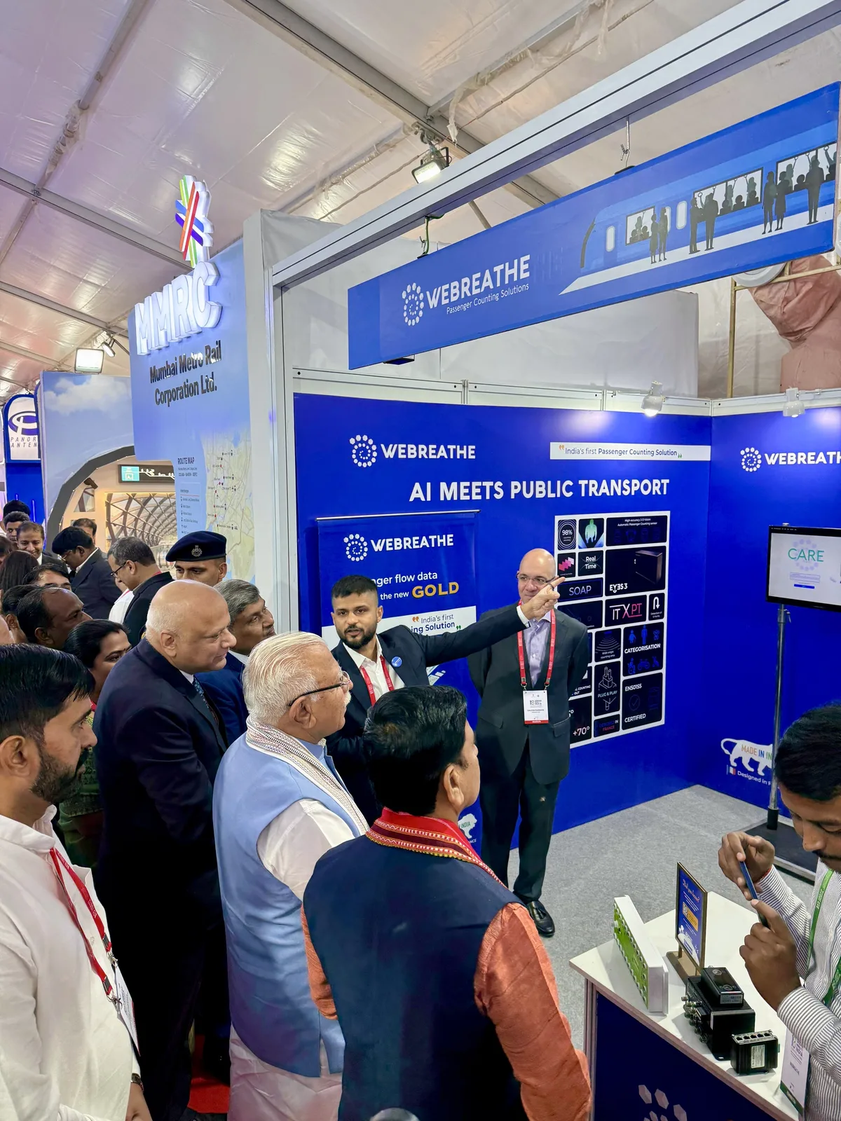 Presenter pointing to an AI Meets Public Transport display as visitors gather at the WEBREATHE booth